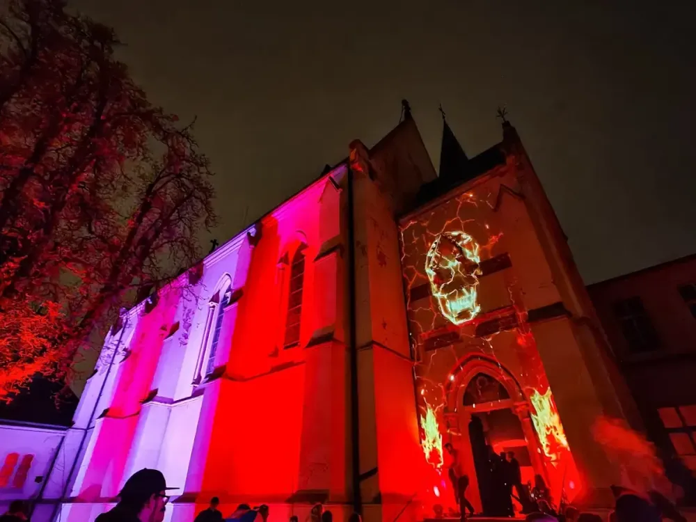 Gothic building lit in red and purple at night, a glowing skull projected above the entrance