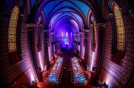 Vaulted hall with stained-glass windows and two long banquet tables lit in blue and purple